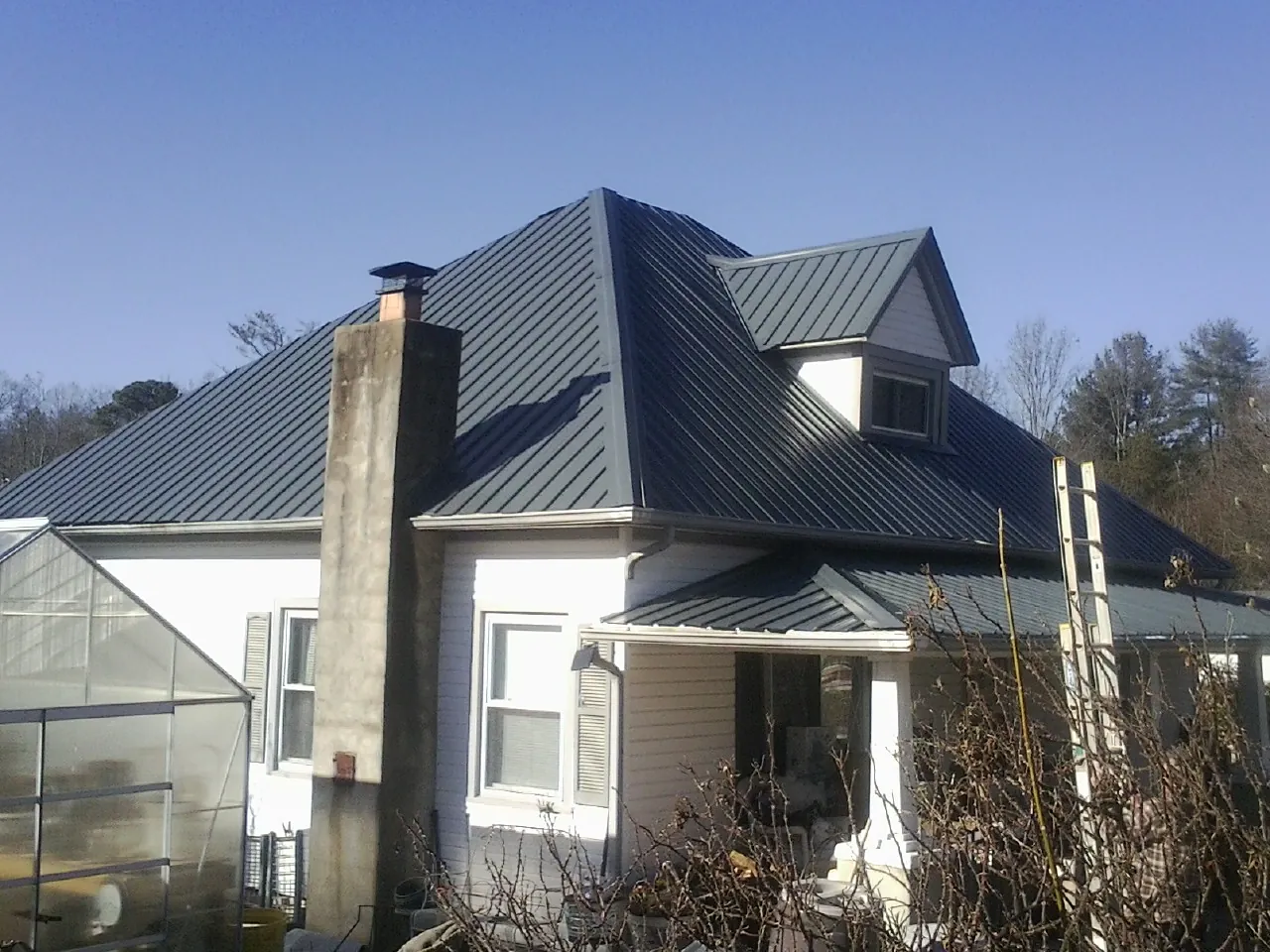 Dark blue standing seam metal roof on a white farmhouse with dormer — Slate & Tile Roof Repair by Roofing Brothers in Georgiana