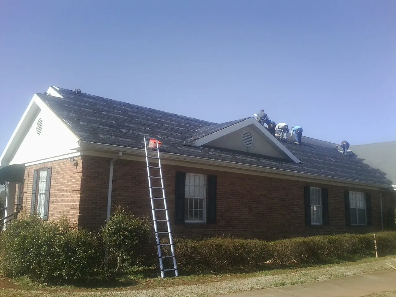 Crew tearing shingles off a brick ranch roof with a ladder set — Emergency Roof Repair work by our crew in Georgiana