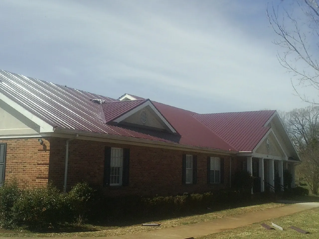 Red metal roof with gabled entries on a long brick building, from a Hail Damage Roof Repair job in Georgiana