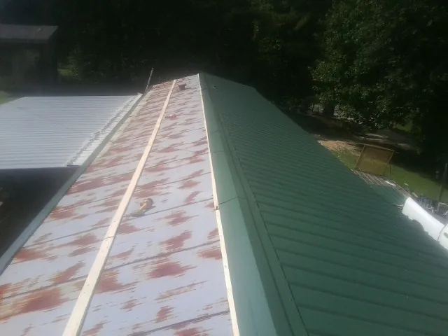 Old rusted panels beside newly installed green metal roofing — Wind Damage Roof Repair by Roofing Brothers in Georgiana
