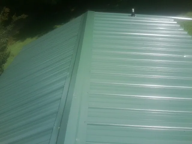 New green metal panels meeting at the ridge of a roof — Flat Roof Repair work by our crew in Georgiana