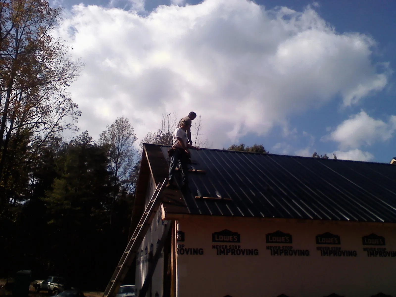 Roofer fastening dark metal panels high against a cloudy sky, from a Roof Inspection job in Georgiana