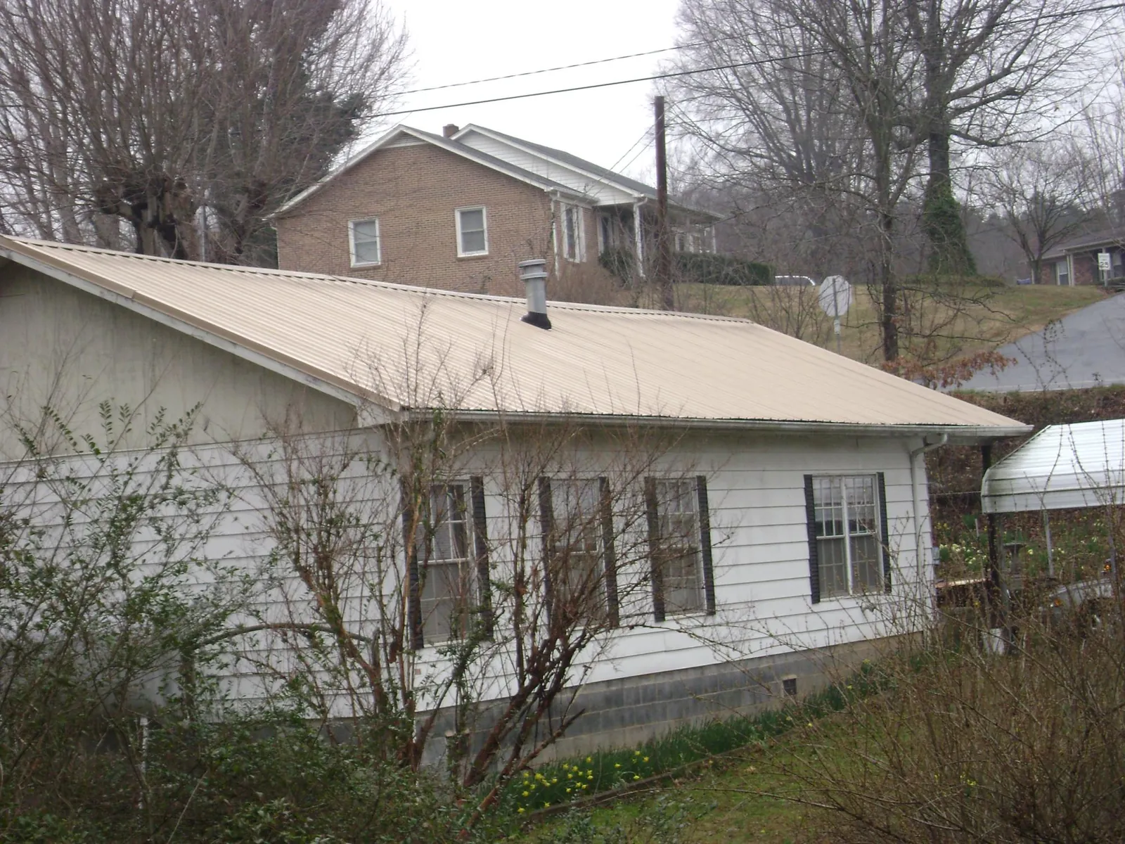 Tan metal roof on a white sided house set into a hillside — Commercial Roofing by Roofing Brothers in Georgiana